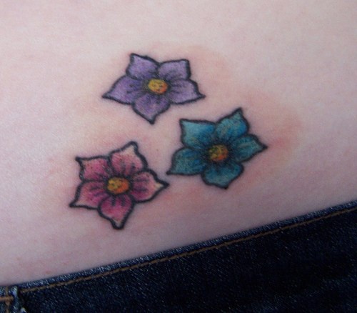 Tatuaje en la cadera, tres flores simples de colores diferentes