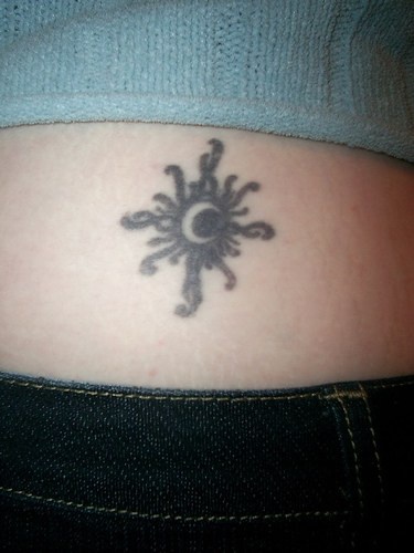 Tattoo von der verschnörkelten schwarzen Sonne in Schwarz mit weißem Mond in der Mitte an der Hüfte