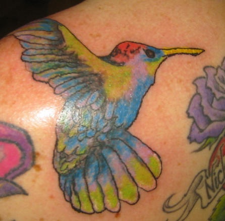 Tatuaje multicolorado de un colibrí volando entre las flores