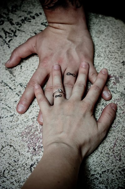 Tuatuaje del s&quotimbolo del infinito en los dedos anulares de una pareja
