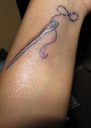 Tatuaje de una aguja con un hilo haciendo el símbolo del infinito