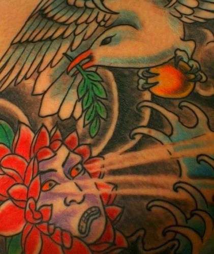 Tatuaje de un pajaro con la hoja en el pico y una cara mitologica