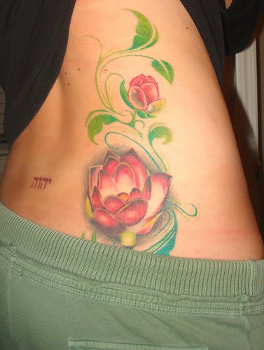 el tatuaje de unas flores de loto en color rosa y hojas verdes hecho en el costado