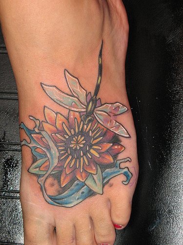 el tatuaje de una flor de loto con una libelula hecho en el pie
