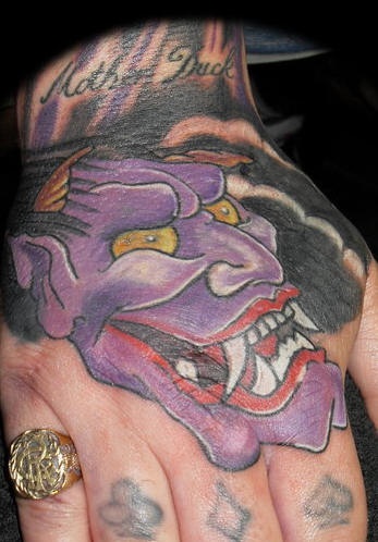 La testa viola di diavolo giapponese che ride tatuata sulla mano