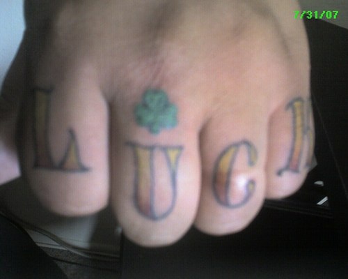 Tattoo &quotLuck" mit kleinem Kleeblatt an Fingerknöcheln