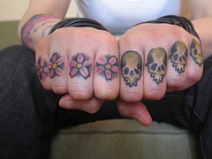 Tatuaggio sulle dita i fiori rosi e i teschi colorati