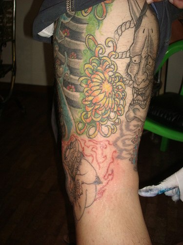 Tatuaggio colorato sulla gamba il teschio annusa  fiore
