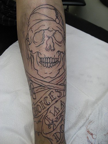 Disegno nero non colorato tatuato sulla gamba il teschio con la scritta
