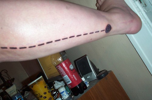 Bein Tattoo, schwarze lange gestrichelte Linie mit schwarzem Kreis