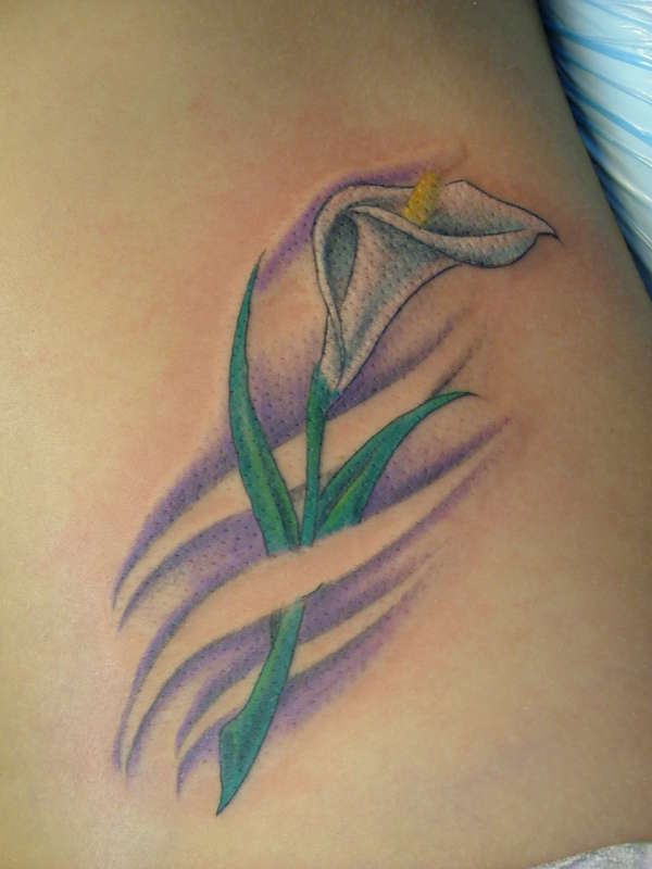 El tatuaje de una pequeña flor de Cala blanca con una lineas cruzandola