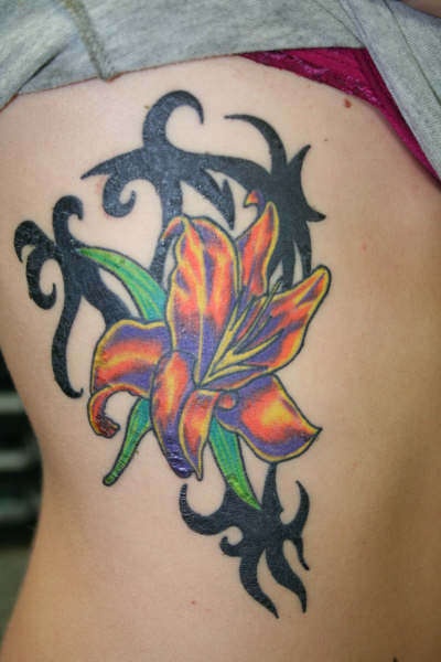 El tatuaje de un Lirio de color naranja y negro rodeado de unas hojas verdes y un entrelazado negro