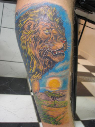 El tatuaje de un leon detallado de color con un paisaje de africa