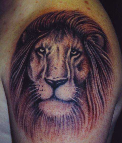 El tatuaje de la cabeza de un leon triste en el hombro