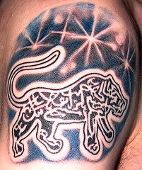 El tatuaje de un leon con estrellas y letras arabes en color hecho en el hombro