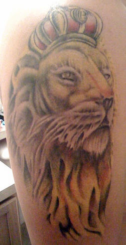 El tatuaje de la cabeza de un leo amarillo con una corona roja hecho en un hombro