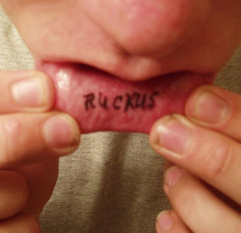 Dünn geschriebenes Tattoo &quotRuckus" in Schwarz  an der Lippe