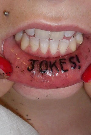 Tattoo &quotJokes" mit Ausrufungszeichen in Schwarz an der Lippe