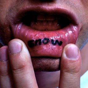 Tattoo mit dicker Inschrift &quotSnow" in Schwarz an der Lippe