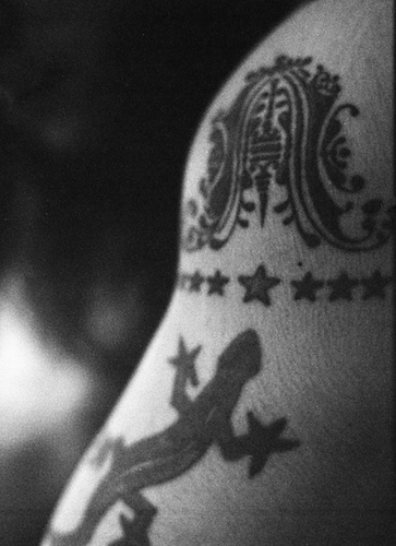 El tatuaje de una lagartija con estrellas y un simbolo en color negro en el hombro o brazo