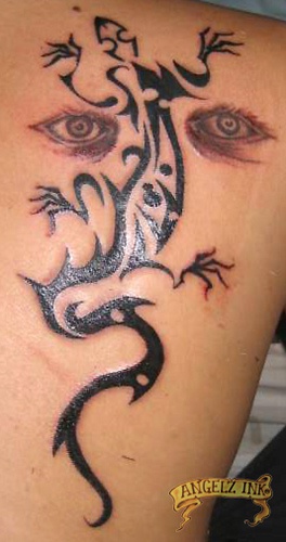 El tatuaje de una lagartija tribal en color negro y ojos humanos en la espalda