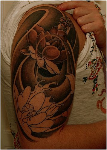 el tatuaje muy bonito de unas flores de loto en olas hecho en el hombro