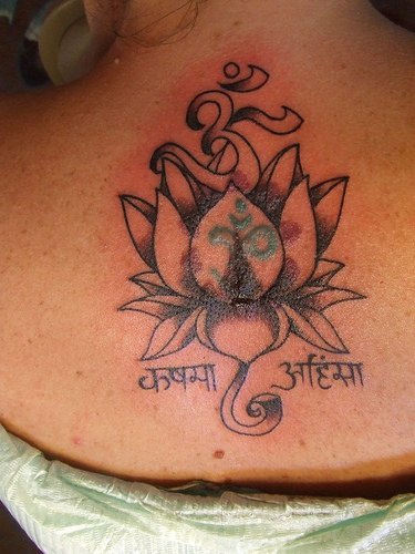 el tatuaje de una flor de loto con mantra om y palabras en hinduhecho en color negro en la espalda