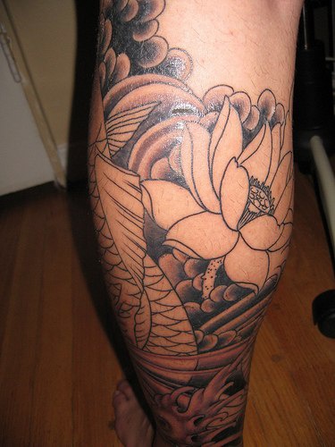 el tatuaje asiatico detallado de una flor de loto hecho en color negro en la pierna