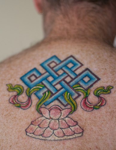 el tatuaje de un nudo de eternidad azul sobre una flor de loto hecho en la espalda