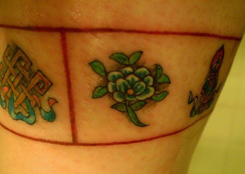 el tatuaje en color de una flor de loto y unos simbolos en forma de brazalete