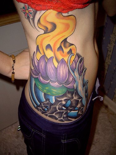 el tatuaje muy vivo de una flor de loto con fuego hecho en el costado