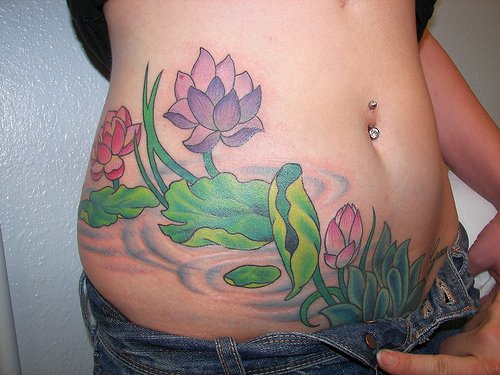 el tatuaje femenino muy bonito de unas flores de loto en el agua hecho en color