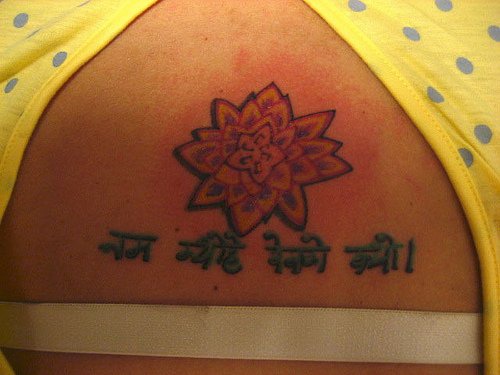 el tatuaje pequeño de una flor de loto con unas palabras en hindu