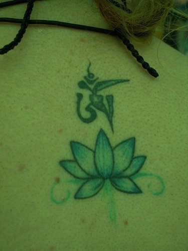 el tatuaje de una flor de loto azul con una mantra hecho en la espalda