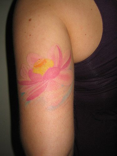 el tatuaje  femenino de una flor de loto de color rosa muy palido hecho en el brazo