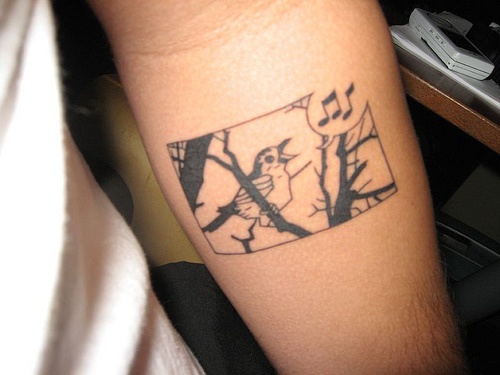 el tatuaje de un pajaro cantando en un arbol hecho con tinta negra