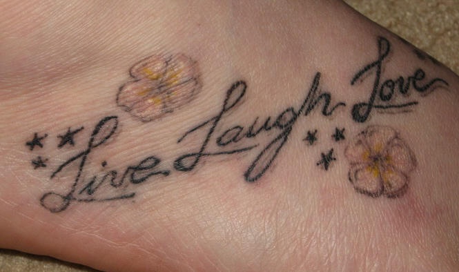 el tatuaje de la frase &quotlive laugh love" &quotvive rie ama" con unas flores hecho en el pie