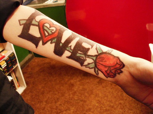 Large love word with red rose tattoo on arm