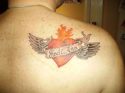 el tatuaje de un corazon rojo con alas y un nombre encima hecho en la espalda