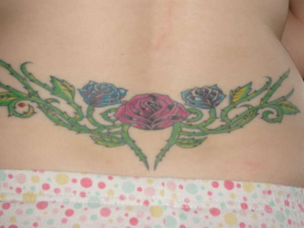 Tattoo am Becken mit rotblauen Rosen in stacheliger Pflanze