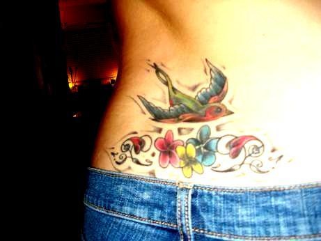 Lower back tattoo, parti-coloured, flying  swallow above flowers