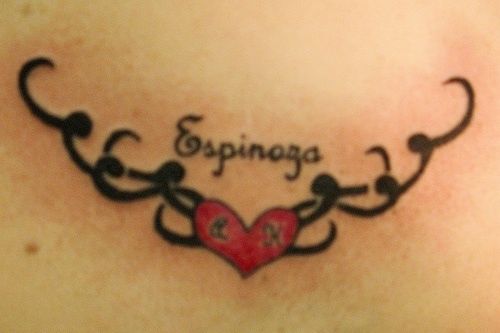 Le tatouage de bas du dos avec un cœur rouge décoré et le mot Espinosa
