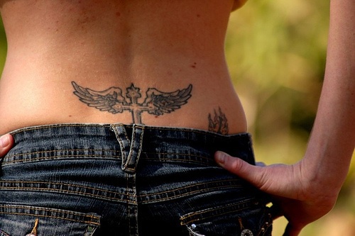 Tattoo mit stilisiertem Kreuz mit Flügeln in Schwarz am Becken