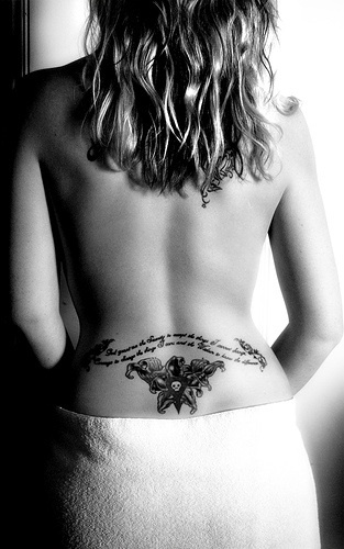 Lower back tattoo, wide text waving and styled skull