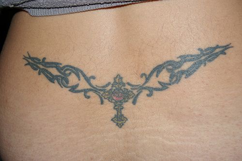 Tattoo von Kreuz mit Stein in geschnörkeltem Muster am Becken