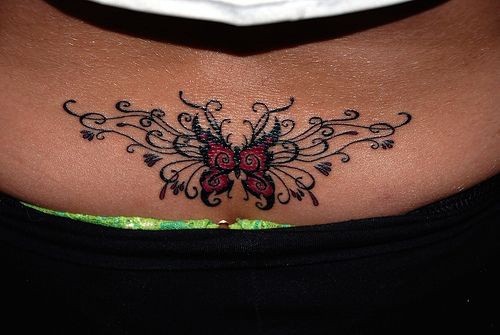 Tattoo mit kleinem schönem Schmetterling in reich geschmucktem Muster am Becken
