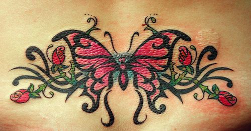 Mariposa con flores alrededor tatuaje en color en bajo de la espalda