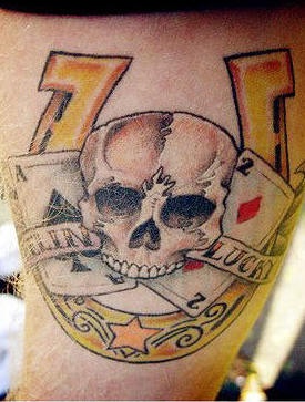 Tatuaje de una herradura, una cráneo y unas naipes