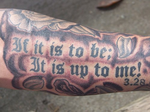el tatuaje de una cita biblica  3:28 hecho en color negro en el brazo