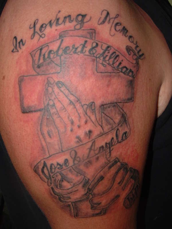 el tatuaje conmemorativo de una cruz y manos orantes  con los nombres en el brazo
